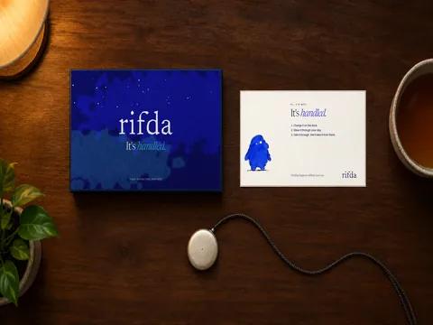The Rifda box, the welcome card with Wafi and the round Rifda pendant on a wooden desk